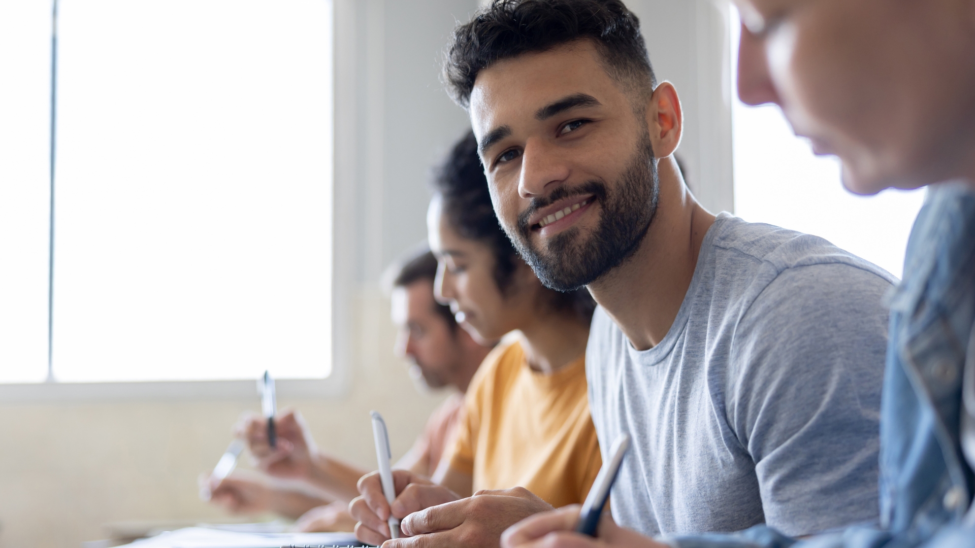 Ein Mann sitzt in einer Reihe mit anderen Studierenden und lächelt