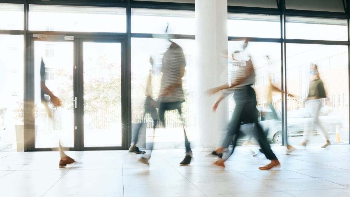 Verschiedene Menschen bewegen sich durch ein Foyer, sie sind durch die Bewegung verschwommen