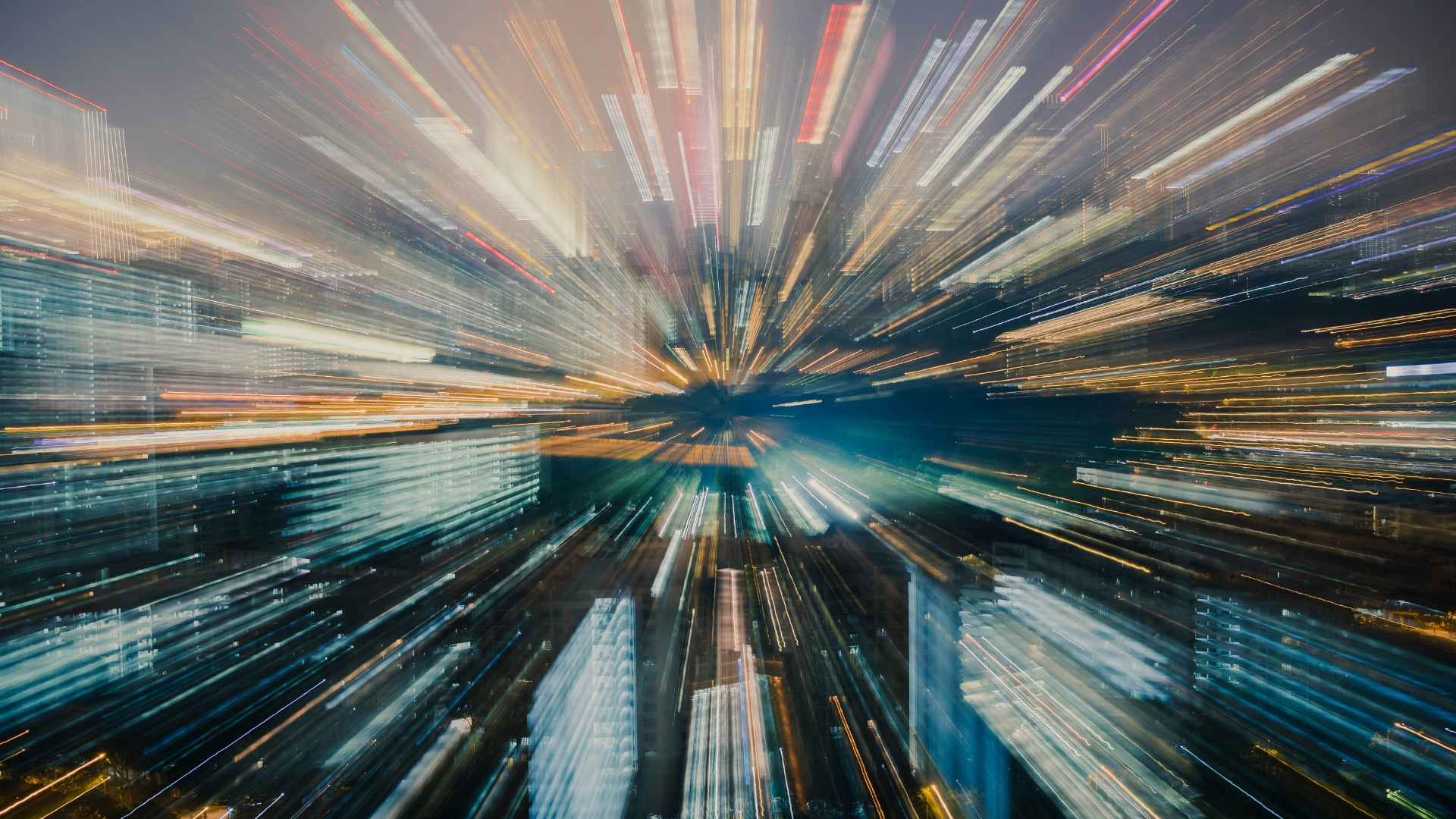 WRBR-Ref_24_Transformation-Digitalisierung-Zukunft - University of Labour Ein dynamisches Bild einer Stadt in Langzeitbelichtung, Umrisse der Stadt sind schemenhaft zu erkennen, verschiede Lichtstreifen haben einen gemeinsamen Mittelpunkt in der Bildmitte.