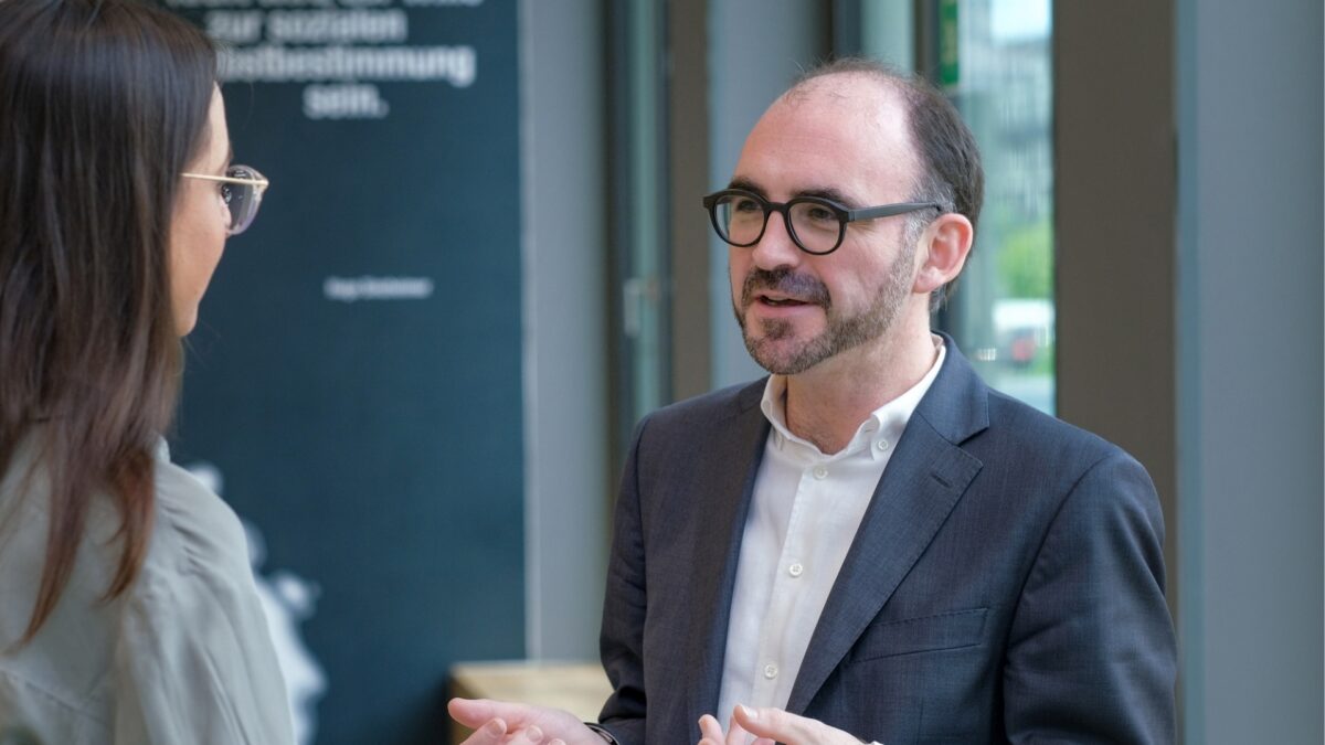 Professor Andreas Engelmann spricht mit einer Interviewpartnerin. Die beiden stehen im Foyer der University of Labour.