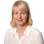 Person_25_Christiane-Kohs1 - University of Labour Porträt einer Frau mit blonden Haaren, die in einem weißen Hemd vor einem weißen Hintergrund lächelt.