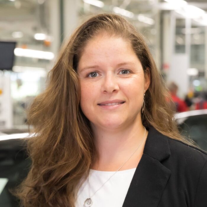Loreen Gabler steht im Mittelpunkt des Bildes. Im Hintergrund ist eine Fabrikhalle von Audi zu erkennen.