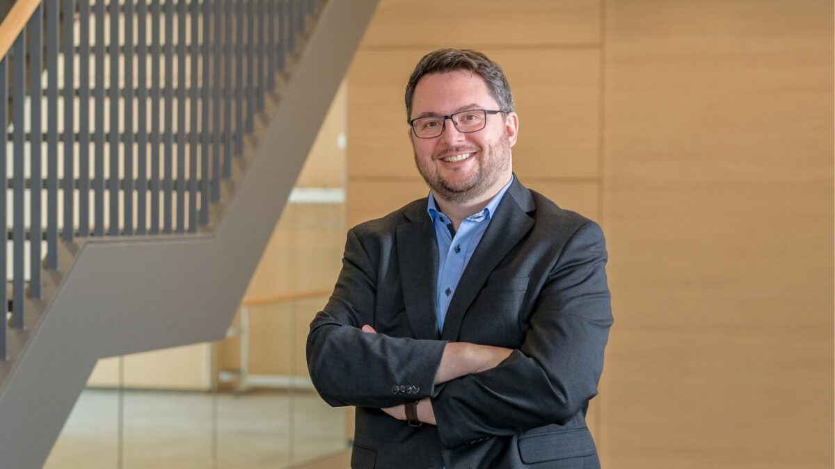 Heiko Hoßfeld steht im Foyer der University of Labour und lächelt selbstbewusst in die Kamera.