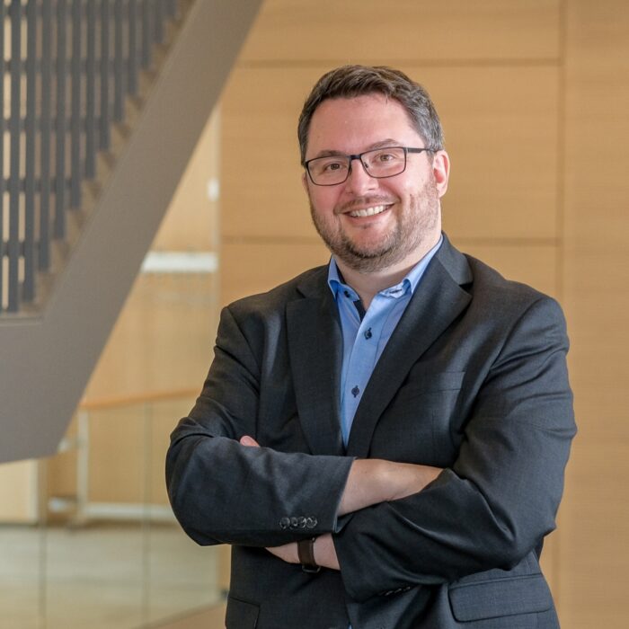 Heiko Hoßfeld steht im Foyer der University of Labour und lächelt selbstbewusst in die Kamera.