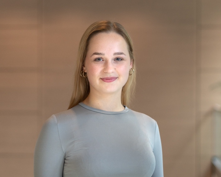 Person_25_Alexandra-Franz - University of Labour Junge Frau mit langen, blonden Haaren und Ohrhängern, lächelt in einem hellen, modernen Raum.