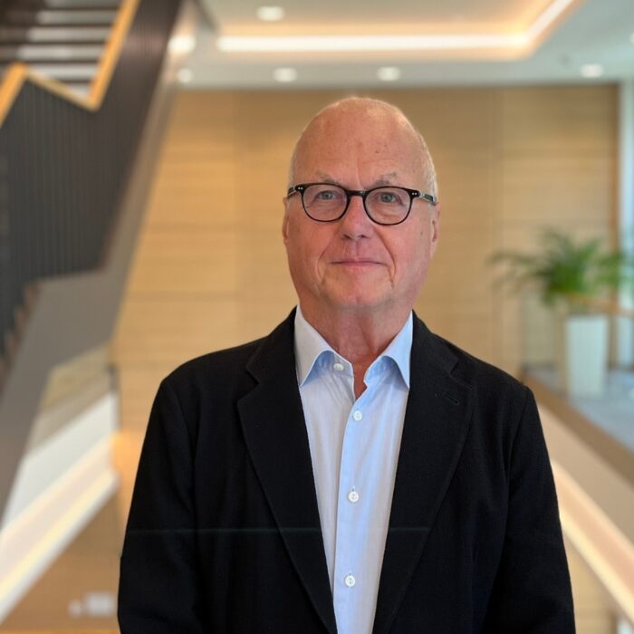 Thomas Klebe mit Brille und Anzug steht in einem modernen Bürogebäude mit Holz- und Pflanzenakzenten, dem Foyer der University of Labour.