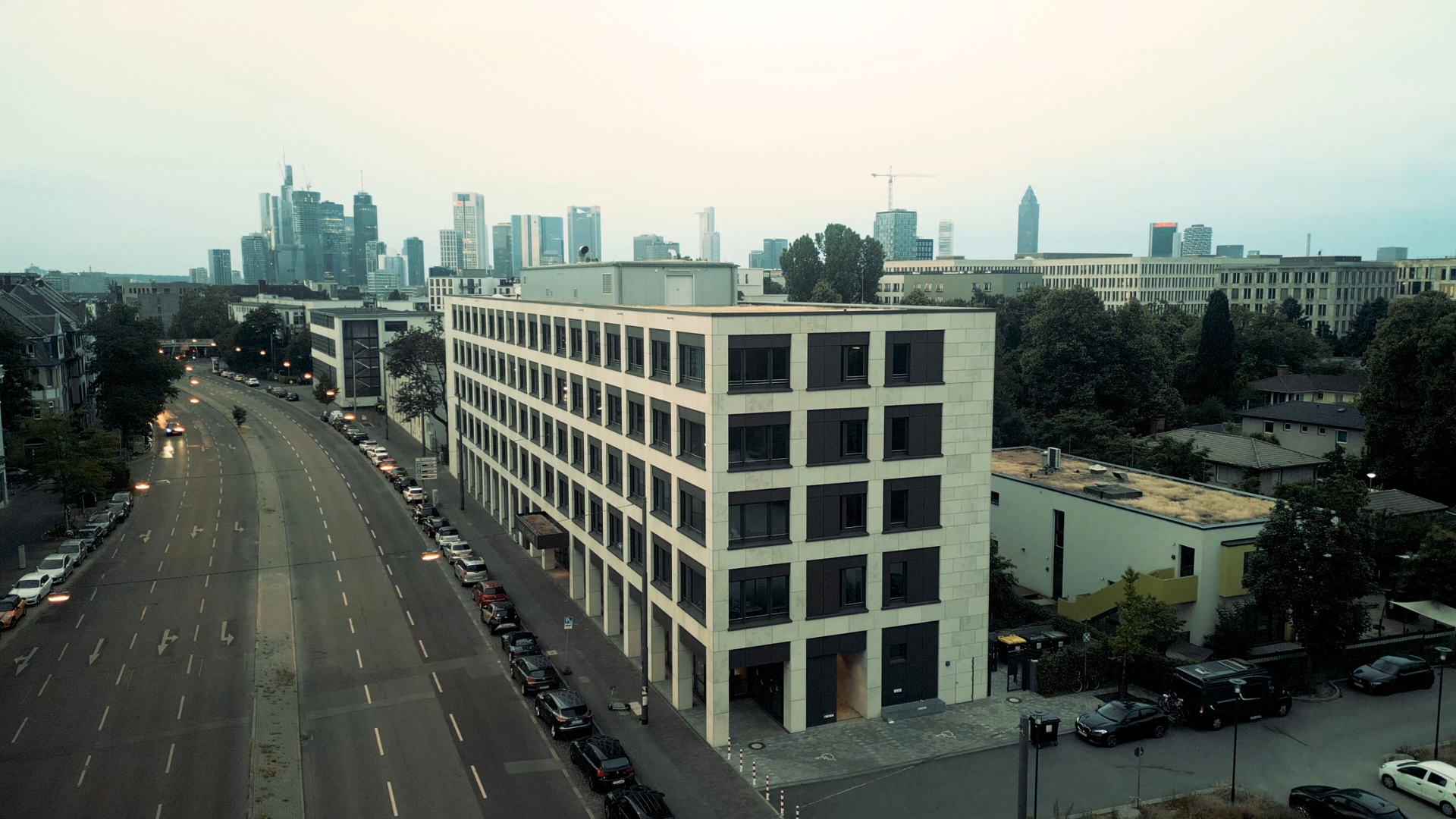 Moderne Gebäude der University of Labour mit Skyline im Hintergrund, umgeben von Straßen und parkenden Autos.