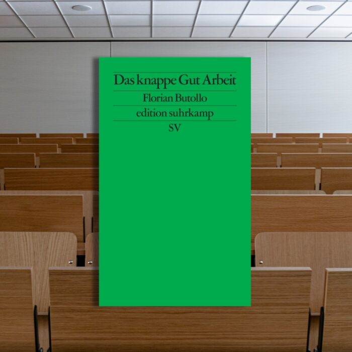 Grünes Buchcover mit dem Titel "Das knappe Gut Arbeit" von Florian Buttolo, platziert vor einem Hörsaal.
